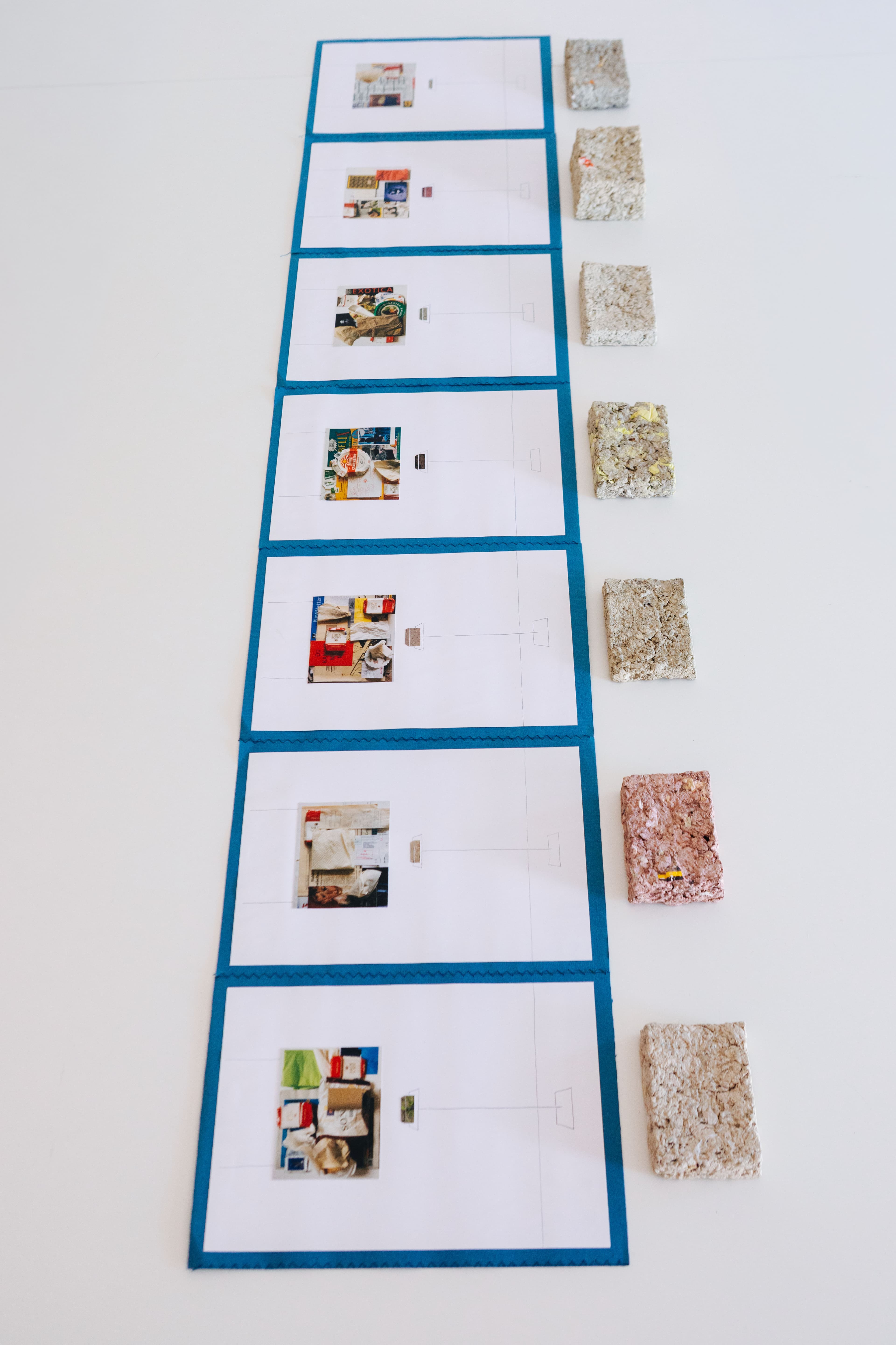 Sieben Tafeln mit Collagen und sieben Papier-Briketts, in Reihe gelegt